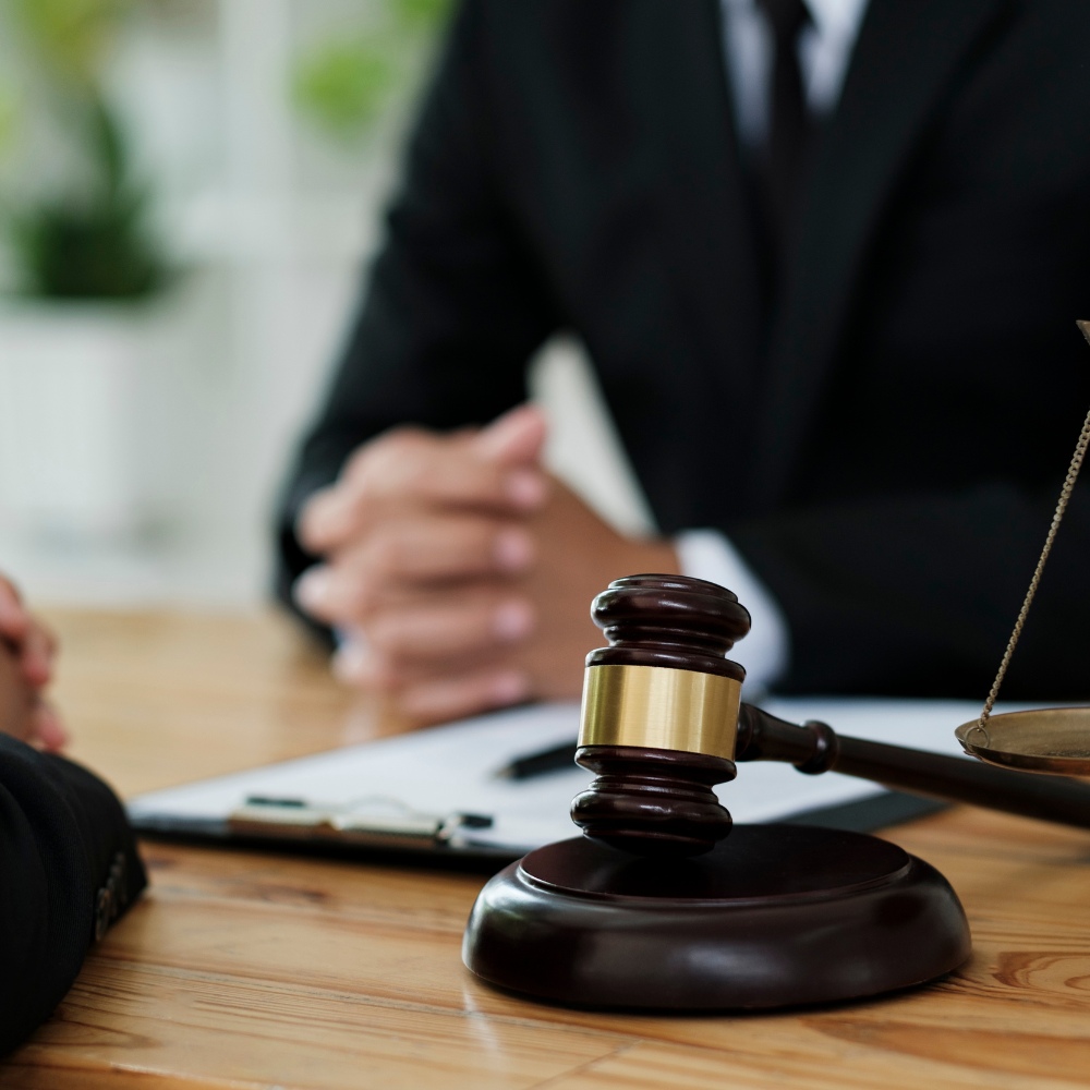 Lawyer consulting with a client in an office with a gavel and scales of justice on the desk.