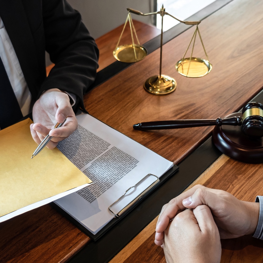 A legal consultant reviews documents with a client, with scales of justice and a gavel on the desk.